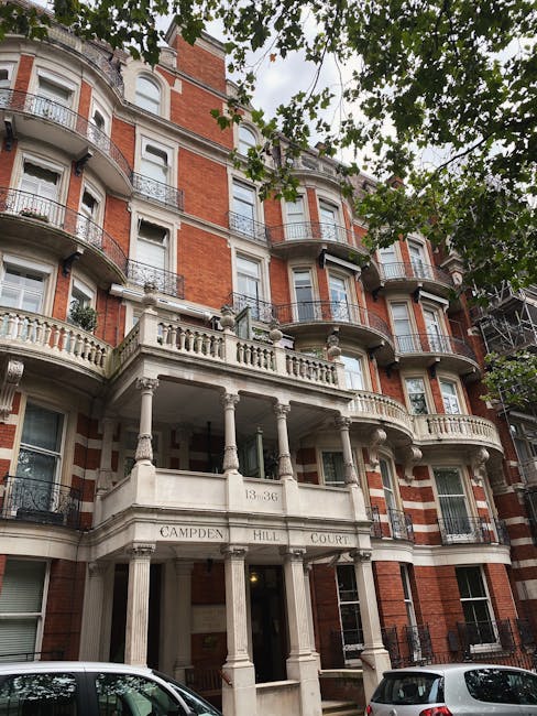 Photograph of a red-brick Victorian terrace on Pembridge Villas in Notting Hill, showing its ornate white stone balcony with decorative balustrades and columns, and multiple large sash windows with wh